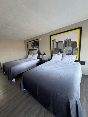 A hotel room with two beds, a cityscape painting, and a lamp.