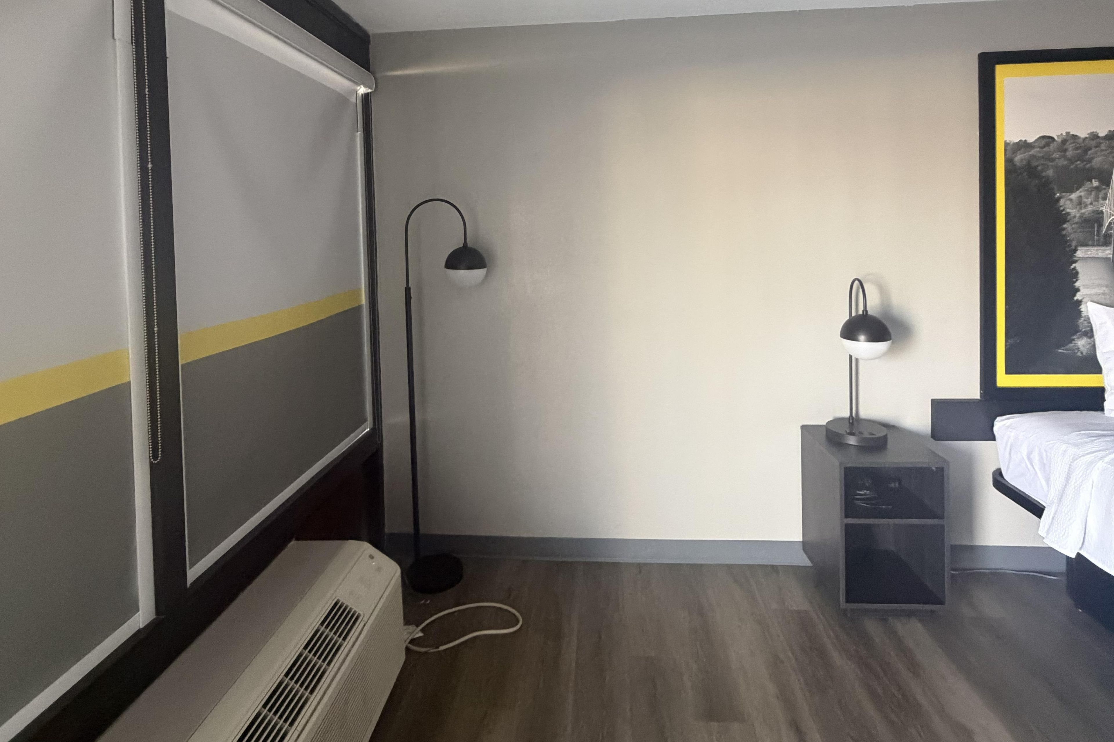 Une chambre d’hôtel équipée d’un lit, d’un bureau, d’une chaise, d’une lampe de sol et d’un radiateur.