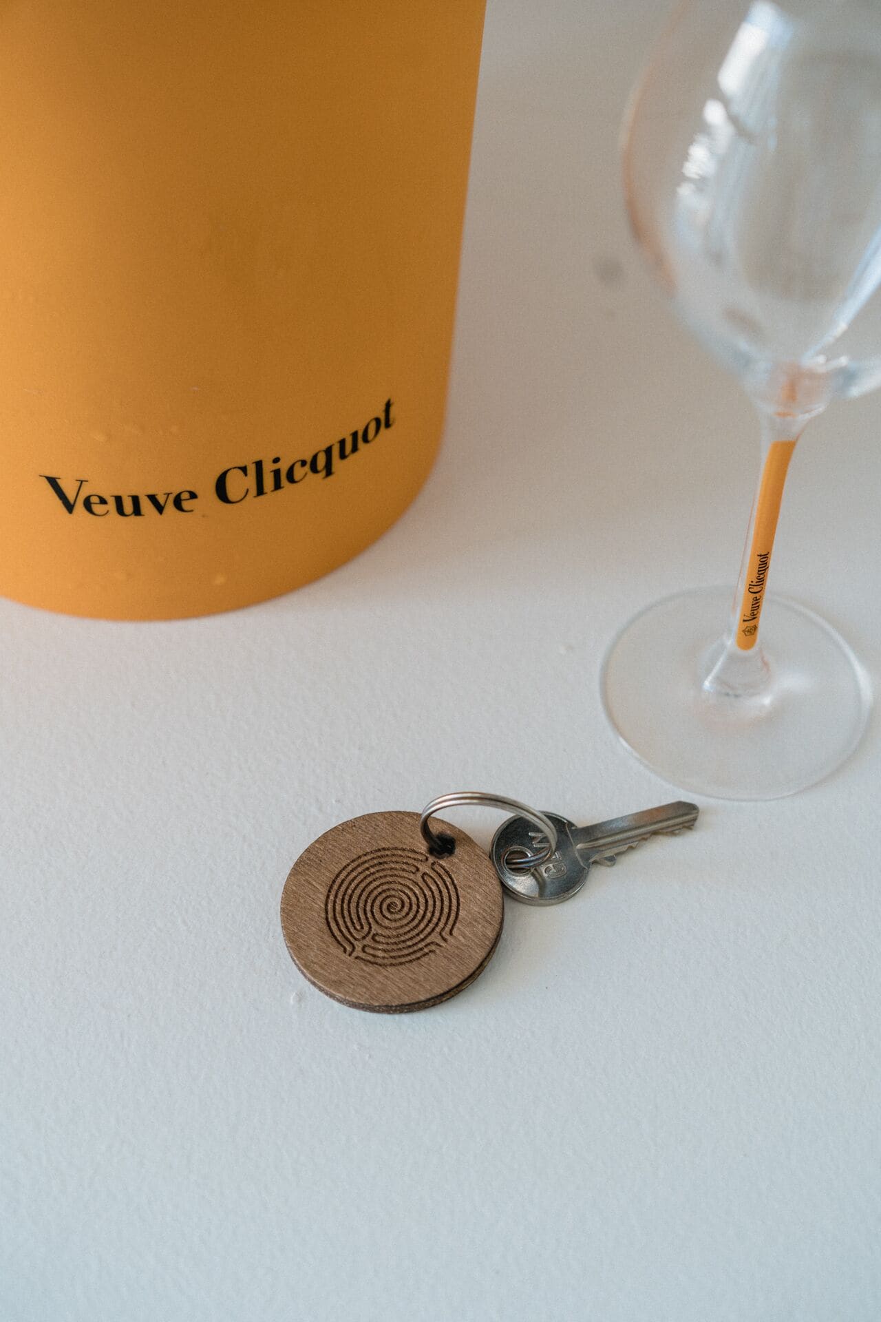 Een fles Veuve Clicquot champagne, een sleutel en een wijnglas op een witte ondergrond.