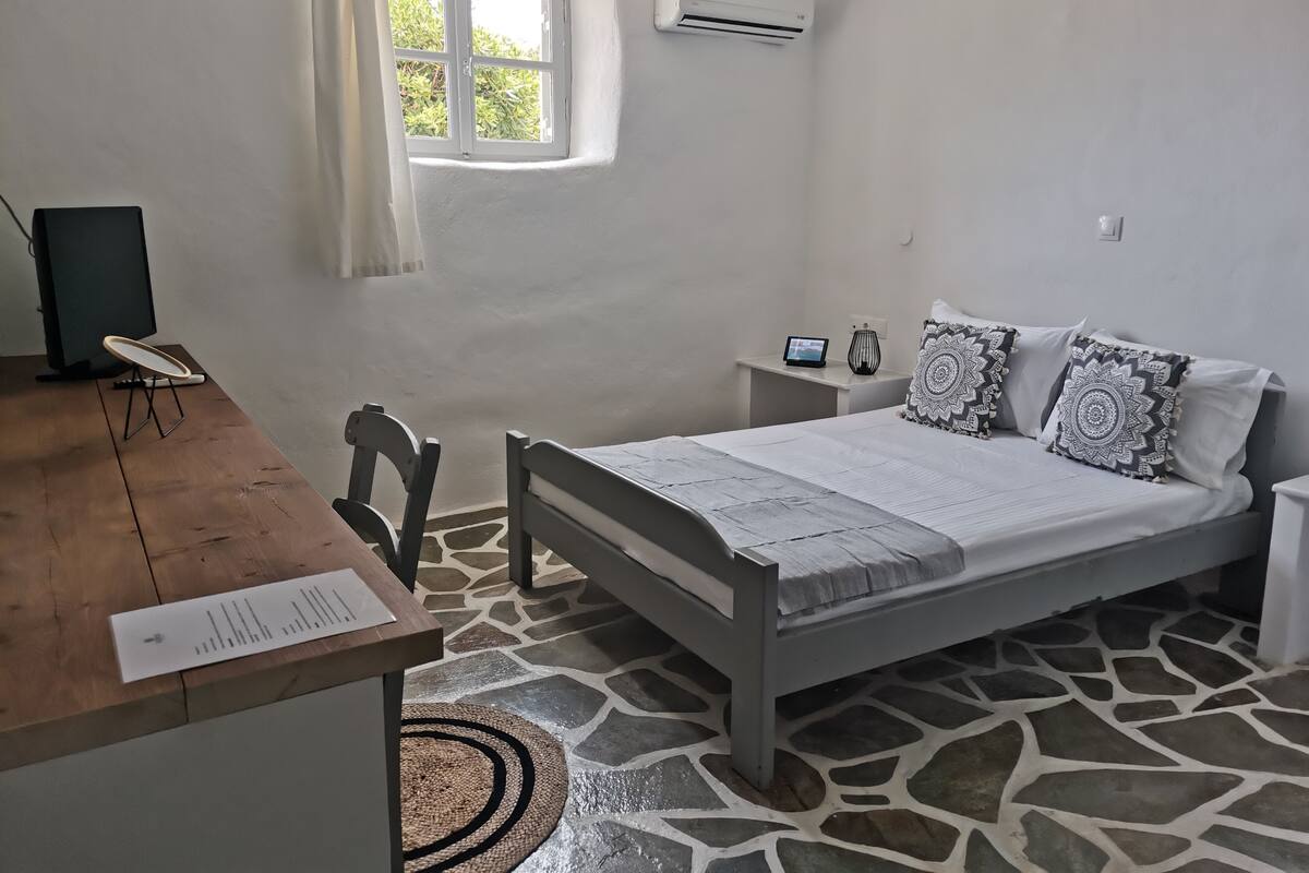 Un dormitorio con cama, mesita de noche, silla, escritorio y ventana con cortinas.