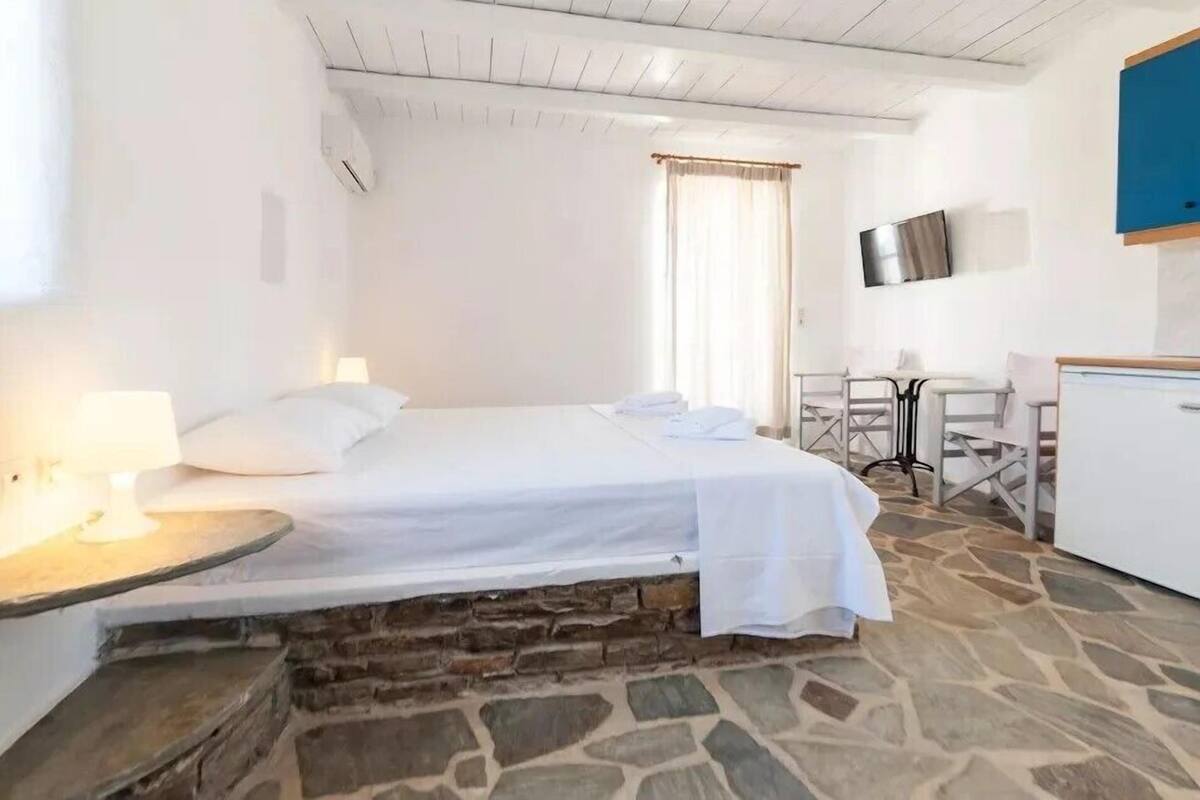 Un dormitorio con una cama, un escritorio, una silla y un televisor en la pared.