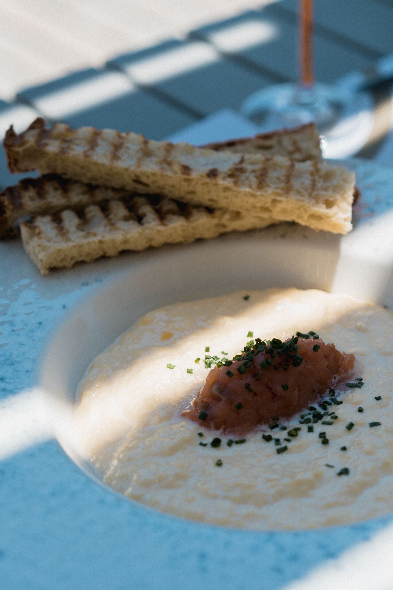 En skål cremet suppe pyntet med purløg, serveret med ristede brødstænger.