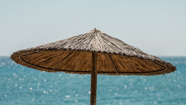 A beach with two wooden chairs and a thatched umbrella. - Soros Beach (Antiparos)