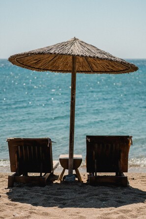 Ein Strand mit zwei Holzstühlen und einem Reetdachschirm.