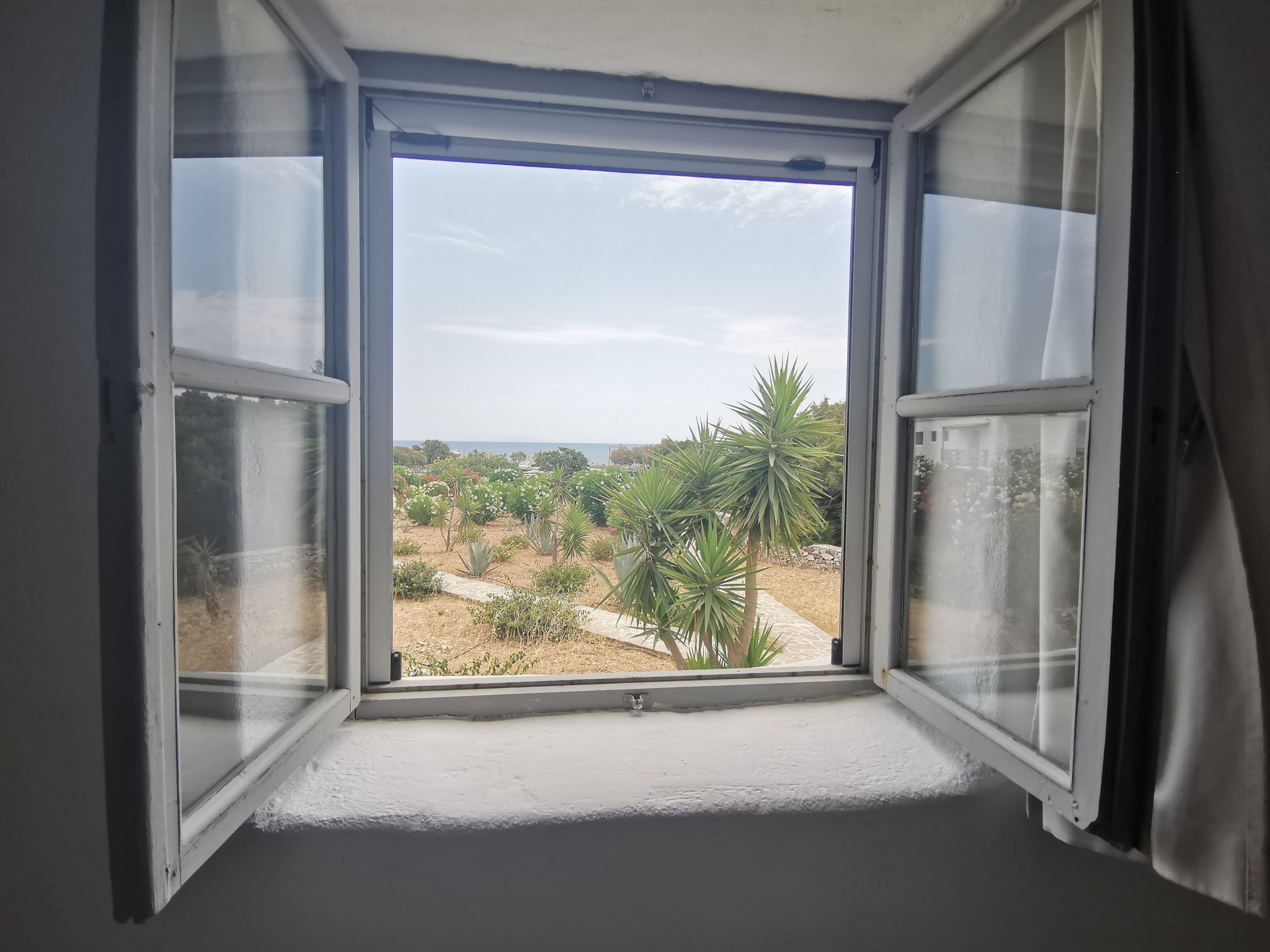 An open window with a view of a garden and a distant landscape.