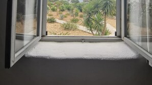A room with an open window overlooking a garden with various plants and a clear sky. - Soros Beach (Antiparos)