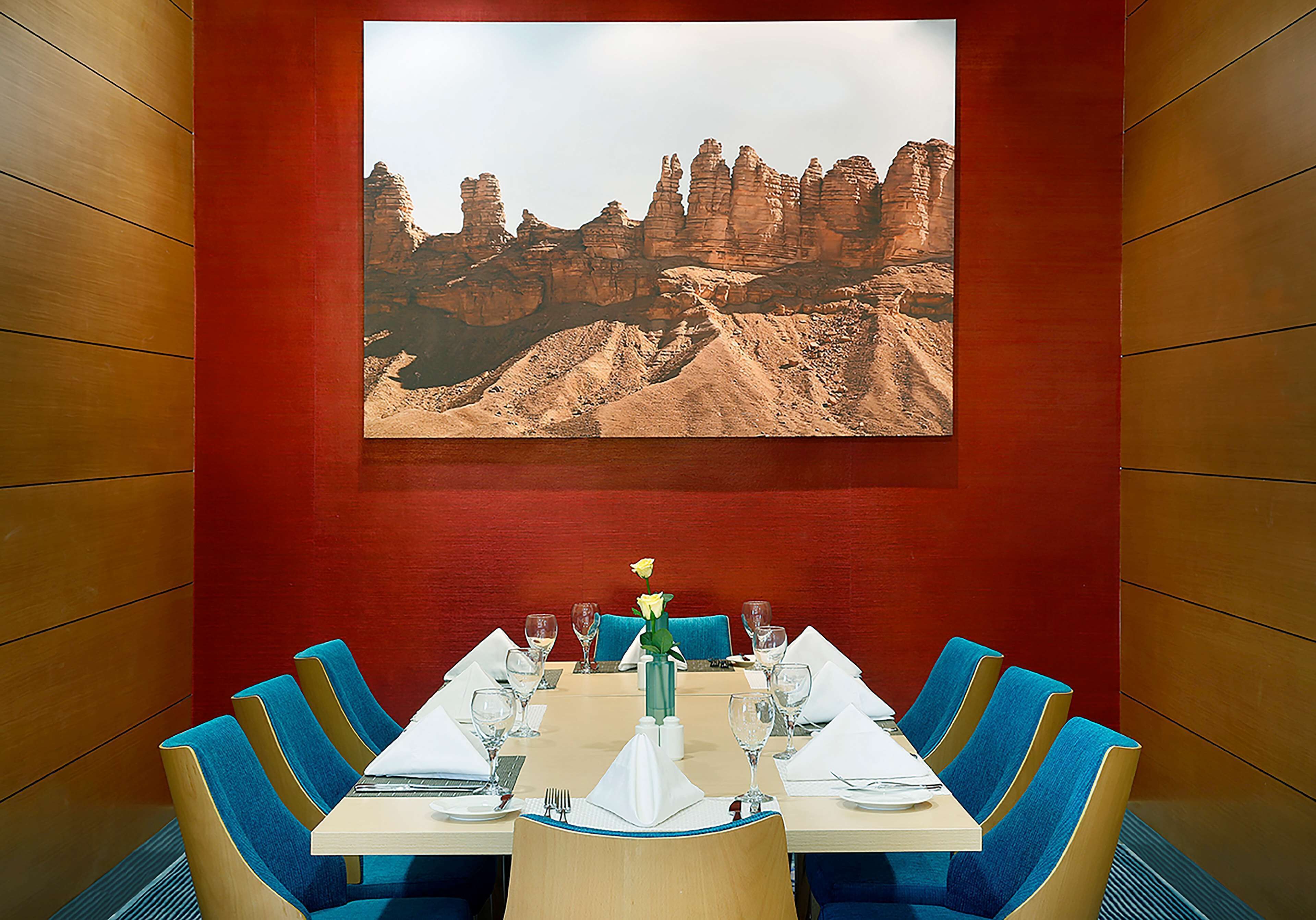 A conference room with a large wall-mounted painting of rock formations, a table set for a meeting, and blue upholstered chairs.