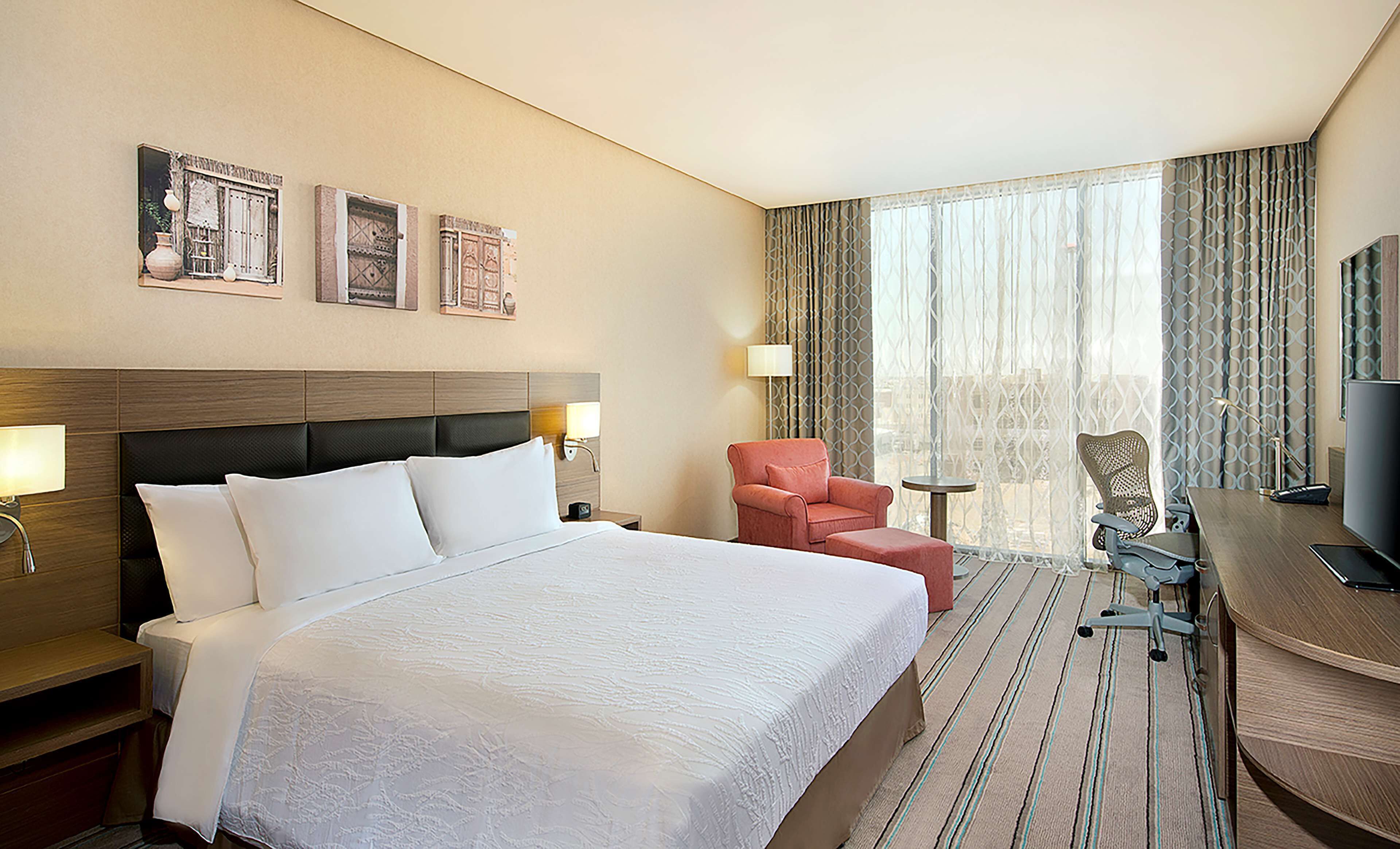 Quarto de hotel com uma cama grande, uma escrivaninha com cadeira, televisão e janela com cortinas.