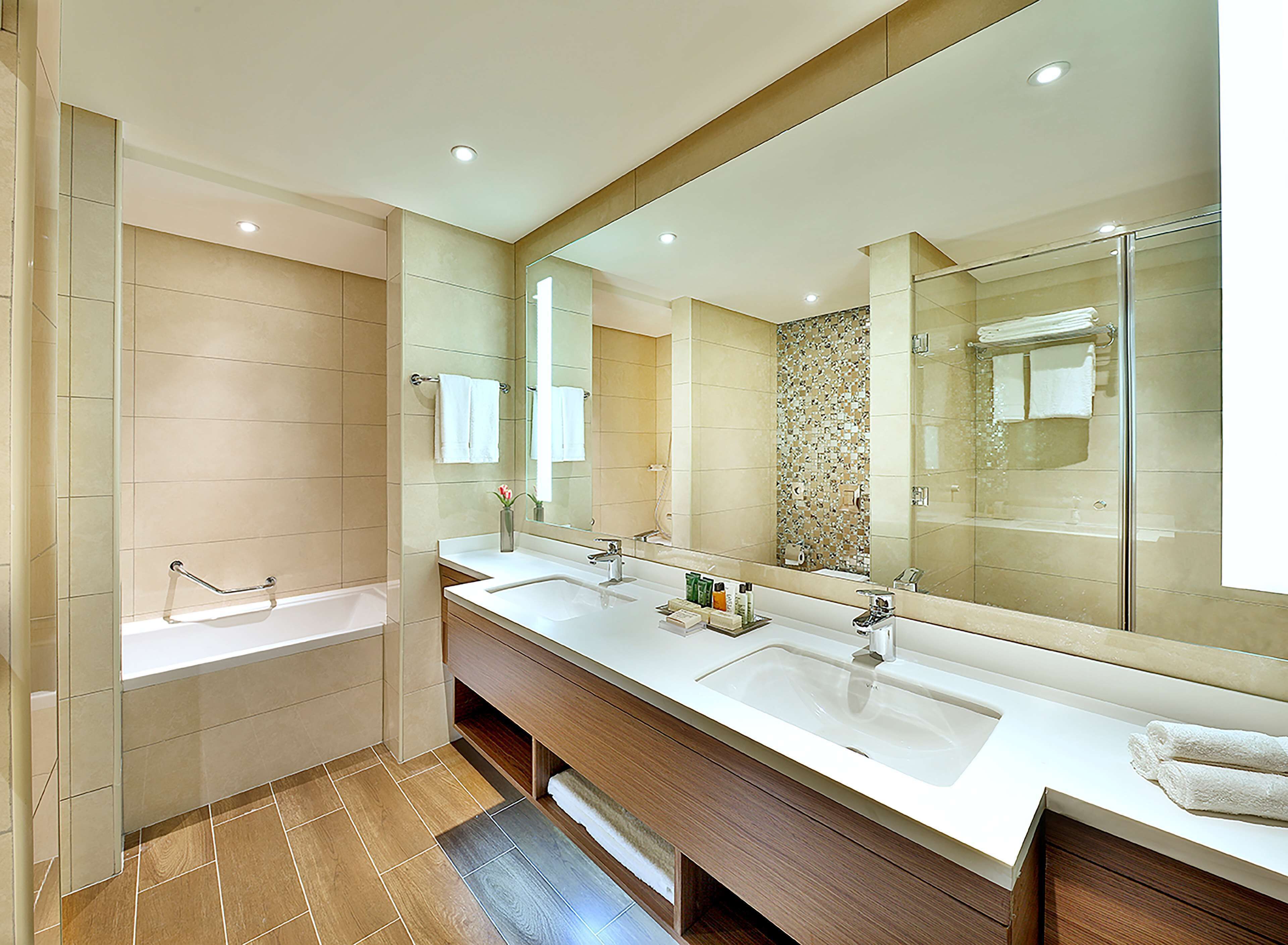 A modern bathroom with two sinks, a large mirror, and a bathtub.