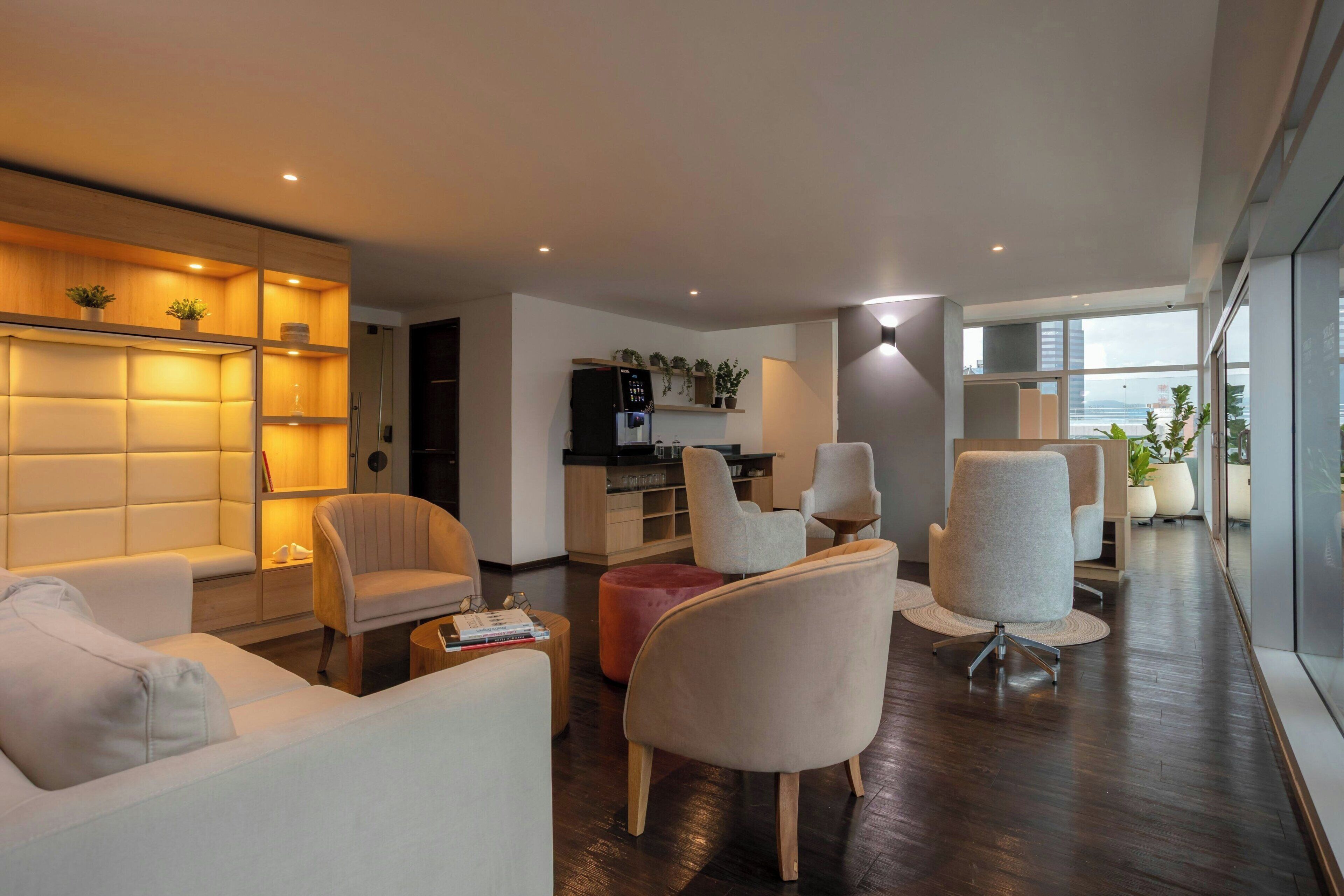 Una sala de estar moderna con sofá, sillones, una mesa de centro y una zona de cocina con refrigerador y dispensador de agua.