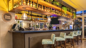 Un espace bar avec un comptoir en bois, de nombreuses étagères remplies de bouteilles, des luminaires suspendus et des tabourets de bar.