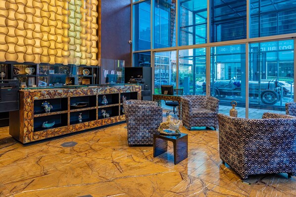 A lobby with a marble floor, patterned sofas, a glass display cabinet, and large windows offering a view of the outside.