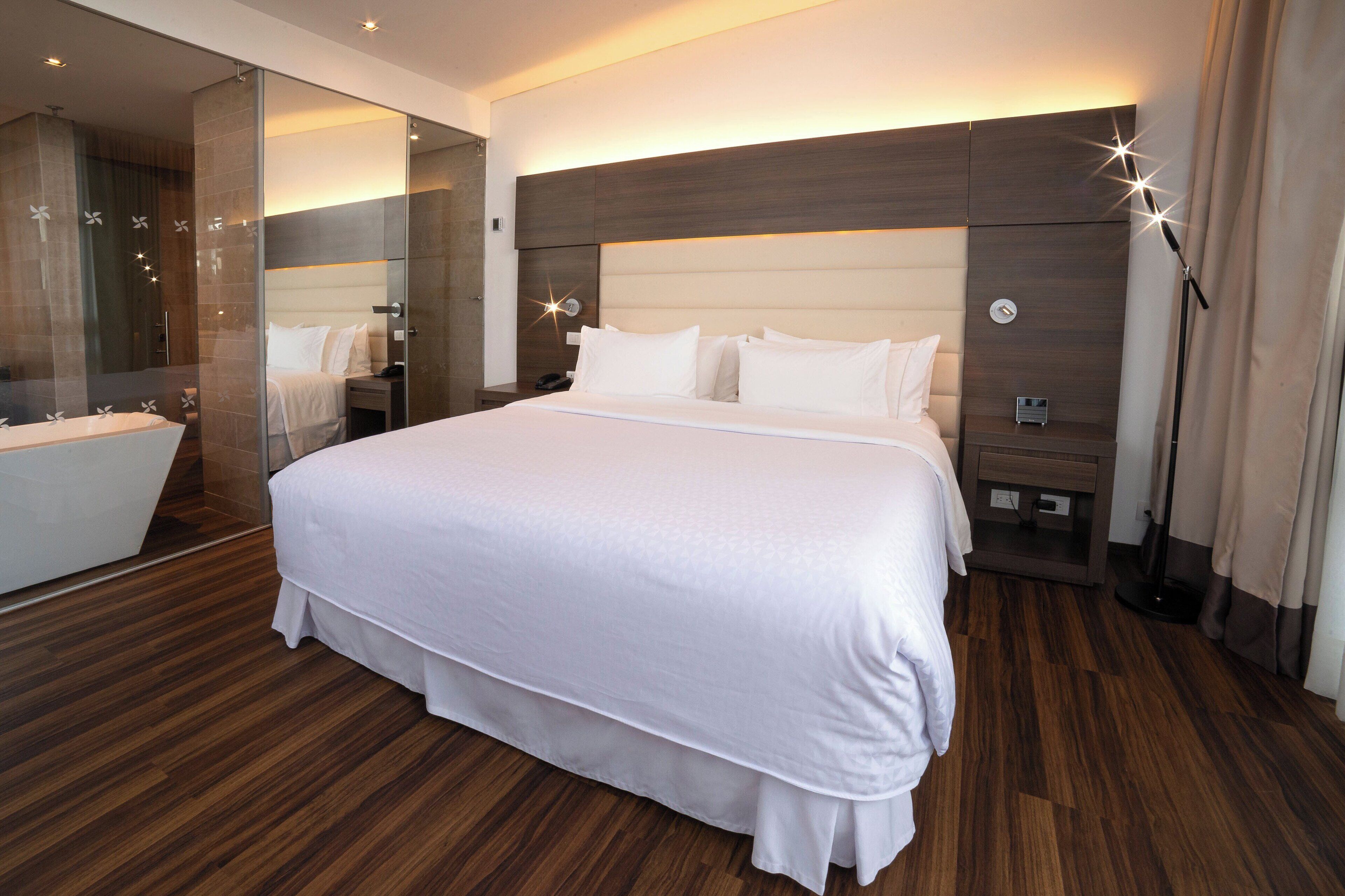 Una habitación de hotel moderna con una cama grande, baño independiente y un espejo amplio.