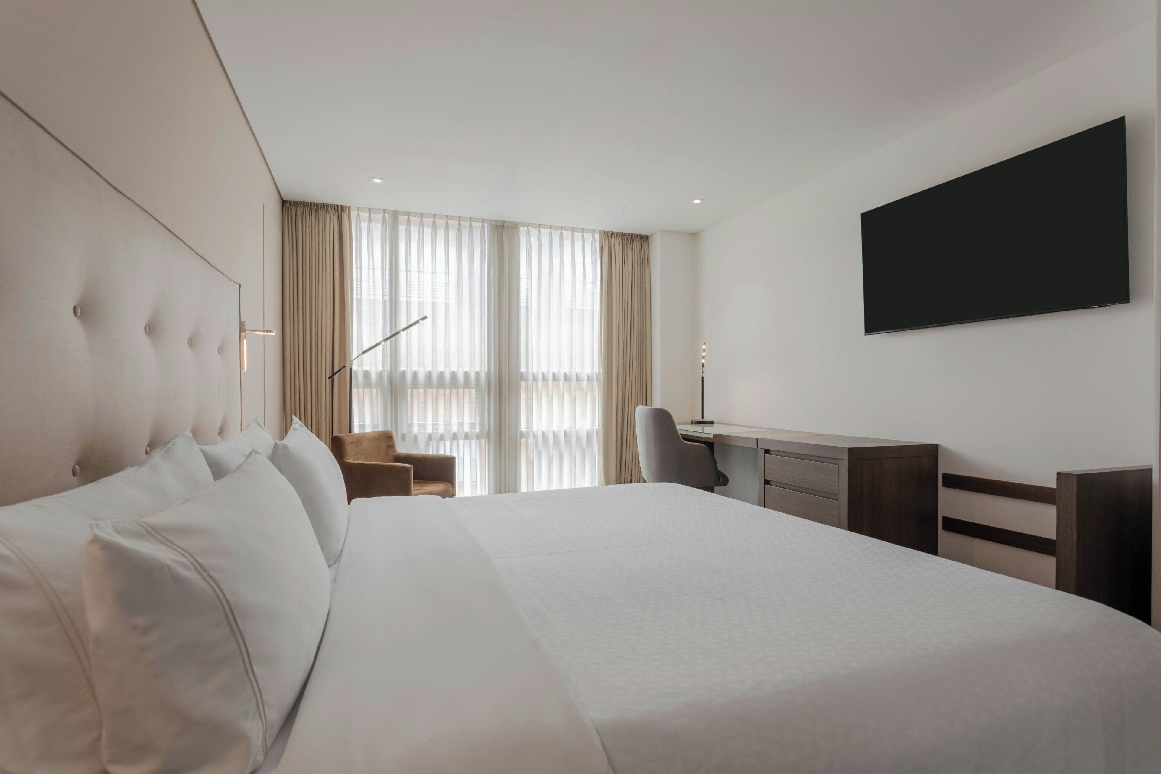 Habitación de hotel con una cama grande, un escritorio, una silla y un televisor de pantalla plana montado en la pared.