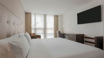 Habitación de hotel con una cama grande, un escritorio, una silla y un televisor de pantalla plana montado en la pared.