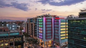 Un hôtel à plusieurs étages, doté d’un design moderne, qui se distingue par une structure verticale imposante, des fenêtres illuminées et une terrasse sur le toit.