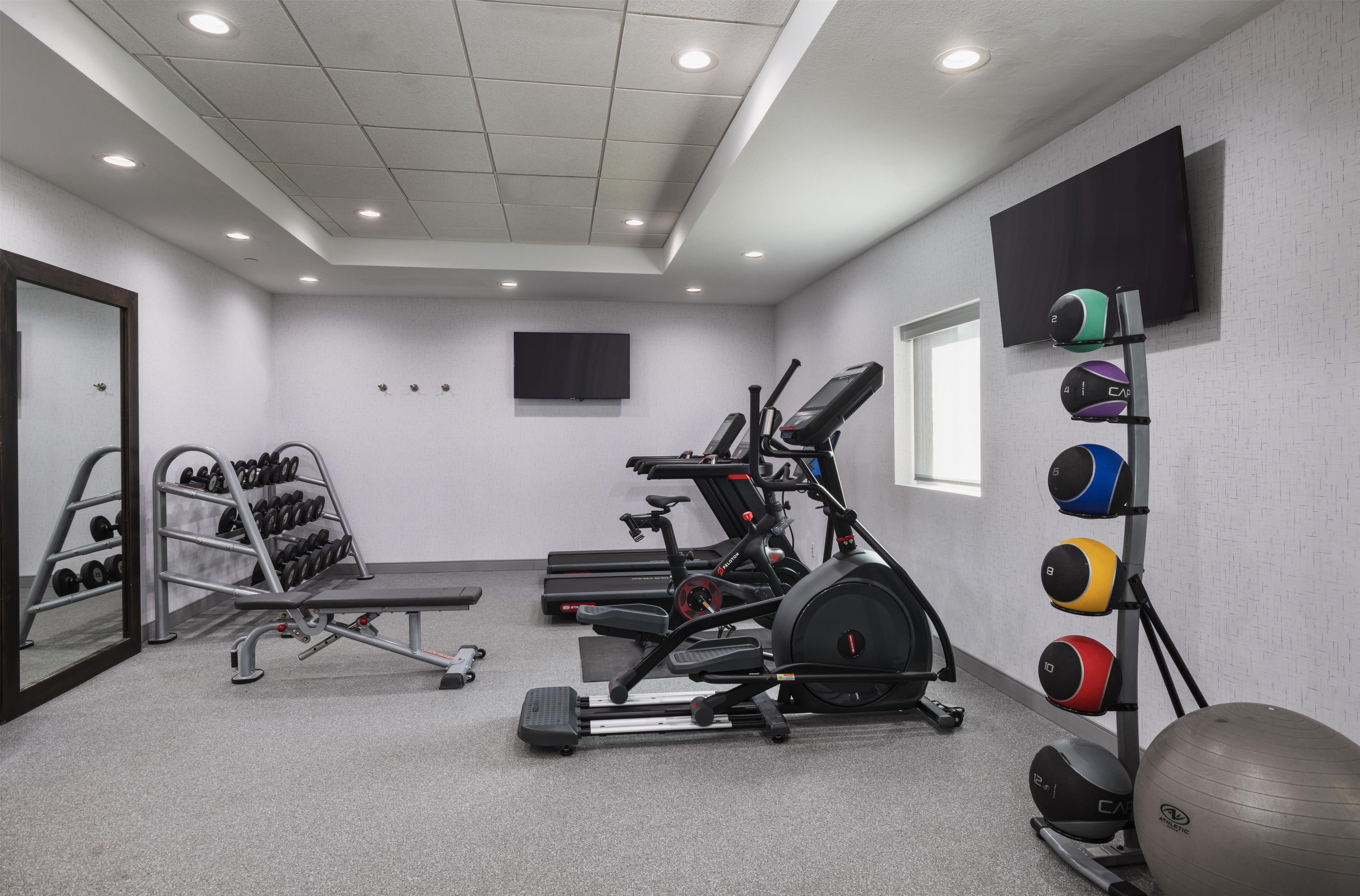 A gym with treadmills, a stationary bike, a weight rack, and a wall-mounted TV.