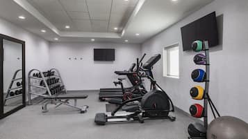 Et fitnessrum med løbebånd, en motionscykel, et vægtstativ og et tv ophængt på væggen.
