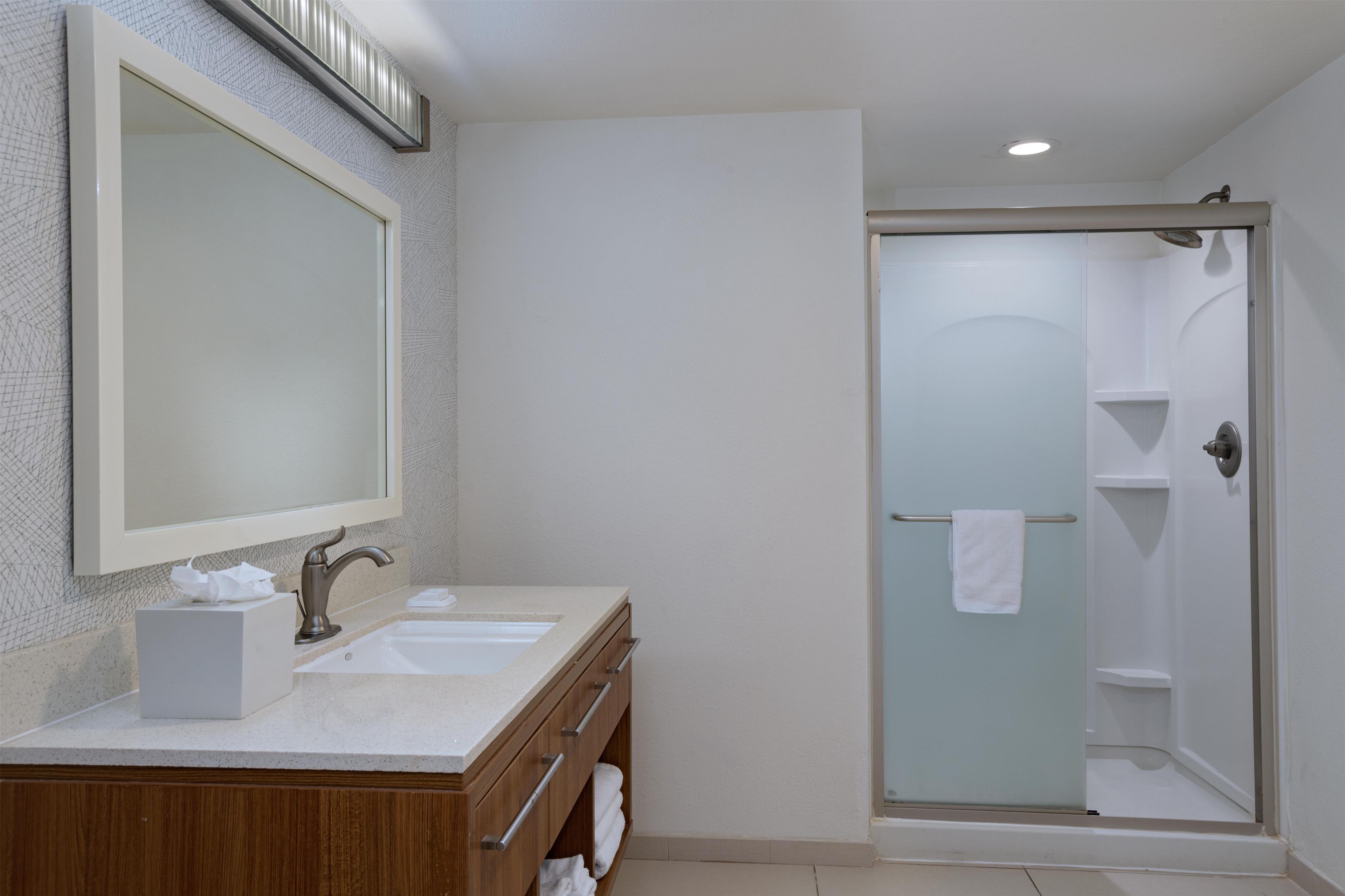 A bathroom with a double sink vanity, a mirror, a towel rack, and a glass-enclosed shower.