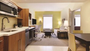 A compact kitchen with a microwave, sink, and coffee maker. A dining area with a table and chairs is visible in the background.