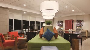 A modern lounge area with green seating, wooden chairs, and a central table.