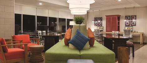 Un espace de détente moderne avec des sièges verts, des chaises en bois et une table centrale.