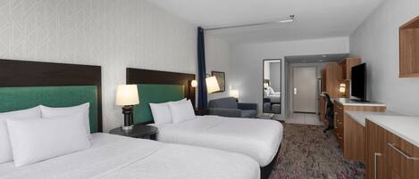 A hotel room with two beds, a desk, a television, and a bathroom visible through an open door.