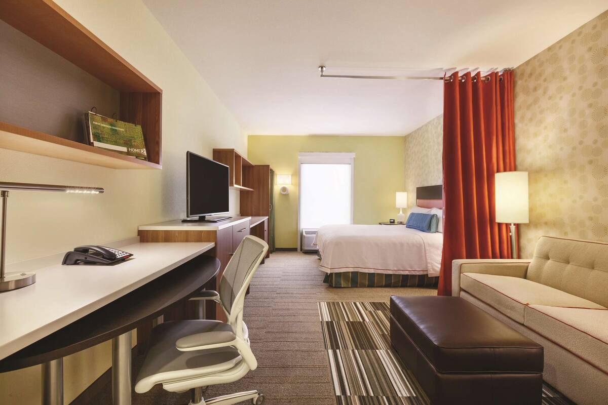 Une chambre d’hôtel équipée d’un bureau, d’une chaise, d’une télévision, d’un lit et d’un canapé.