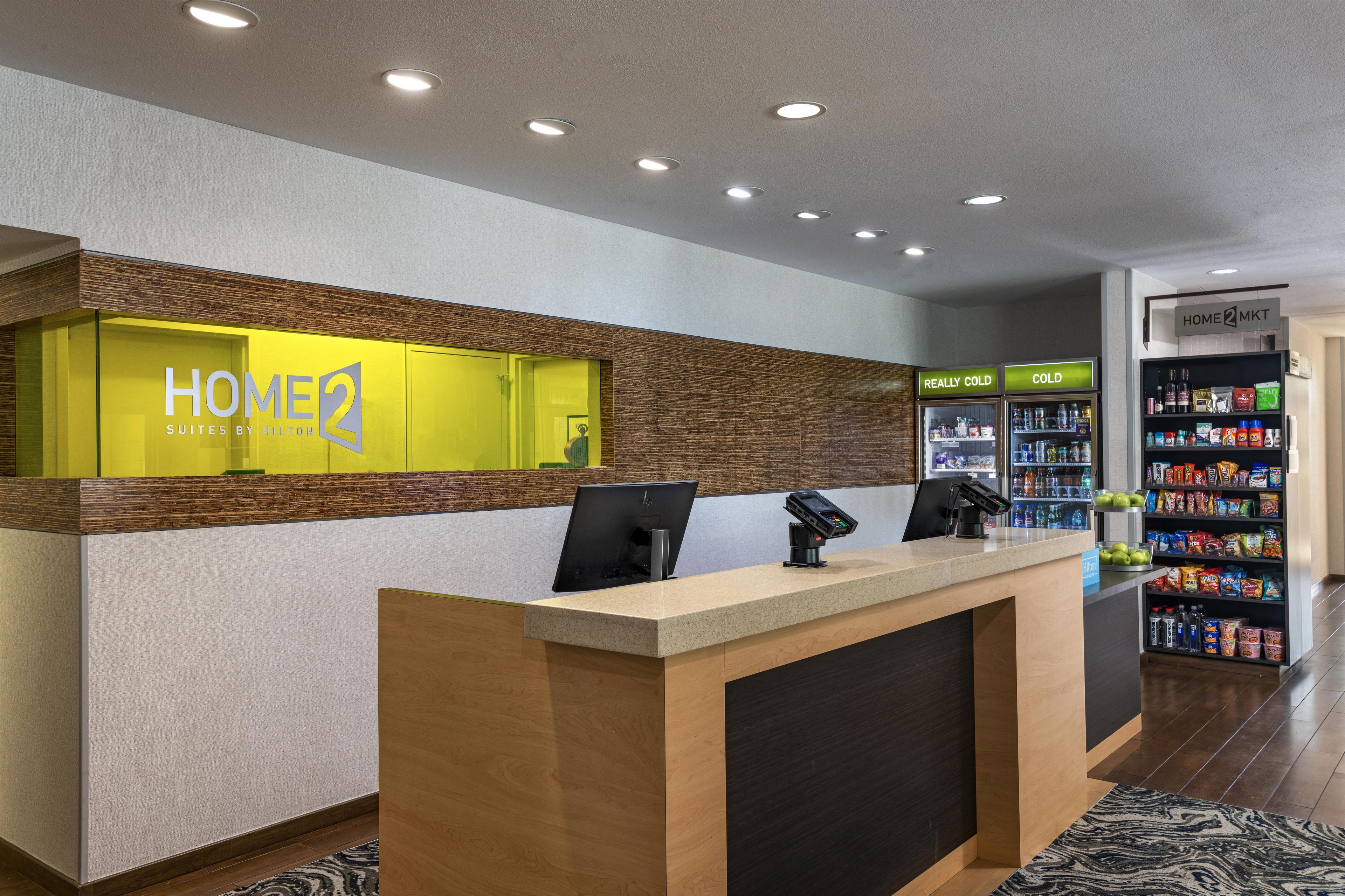 Et hotellets reception med receptionsdisk, minibar og en selvbetjeningsstation for drikkevarer.