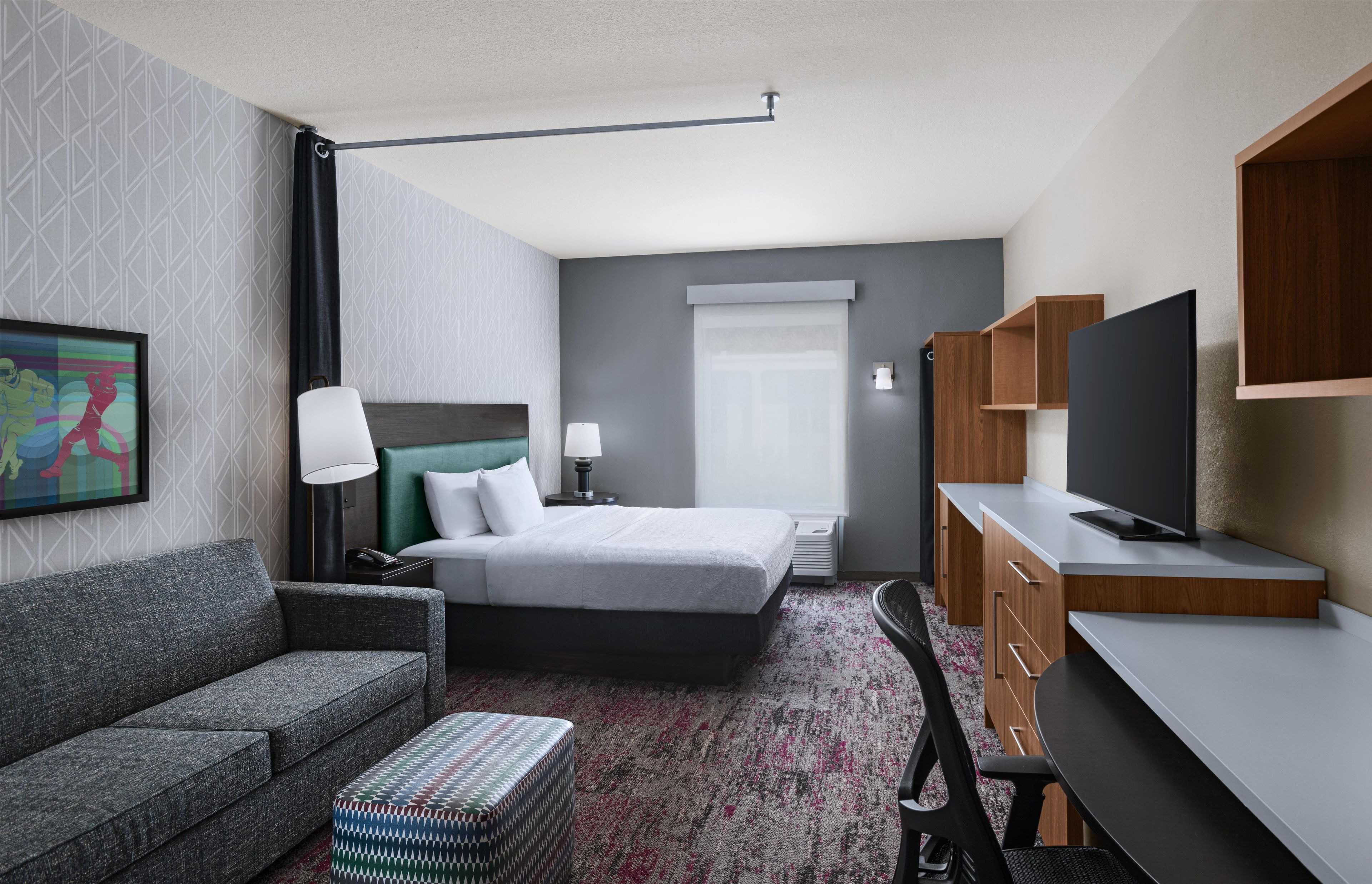 A hotel room with a bed, a sofa, a desk, a television, and a painting on the wall.