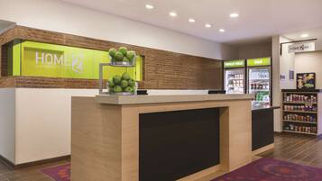 A hotel reception area with a reception desk, a fruit bowl, a minibar, and a beverage cooler.