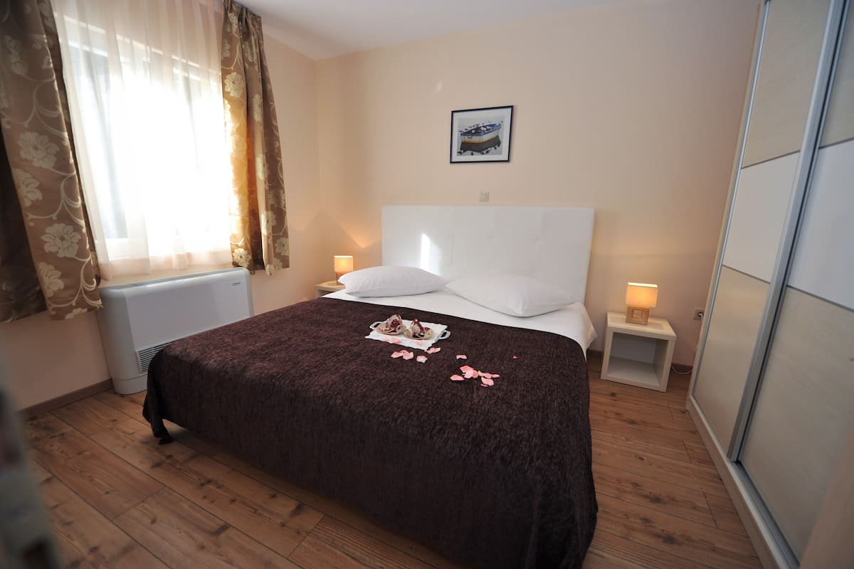 A neatly made bed with a brown blanket, two pillows, and a small table with a lamp beside it.
