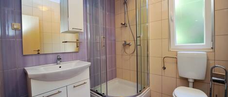 Un baño moderno con ducha de vidrio, lavamanos blanco y retrete.