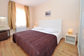 A hotel room with a large bed, a desk, a chair, a nightstand with a lamp, and a window with curtains. - Lastura Aparthotel & Mobile Homes (Novalja)