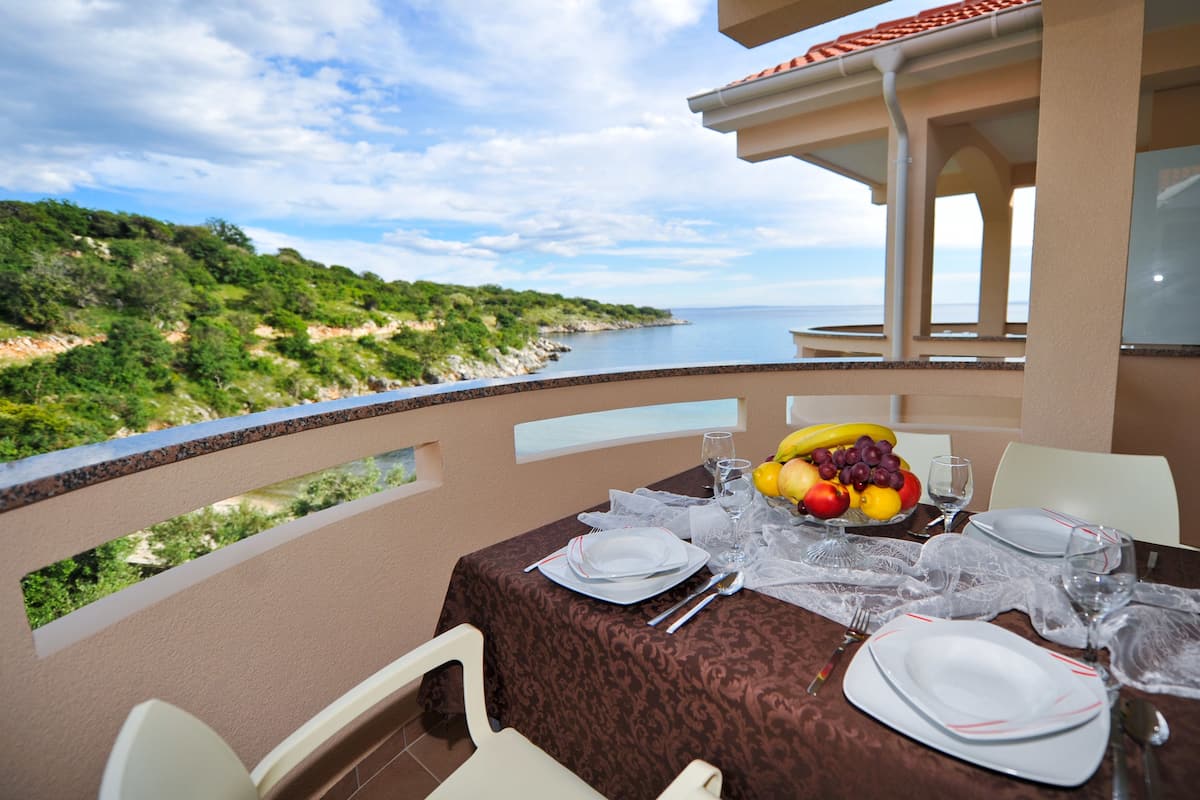 A dining table set with plates, cutlery, and a fruit bowl, overlooking a coastal landscape.