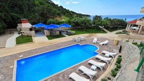 Una piscina con sillas de descanso, zona de barbacoa y vistas al mar.