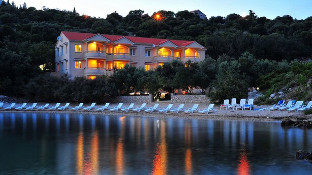 Un hotel de varios pisos con balcones y una zona junto a la piscina con sillones de descanso.