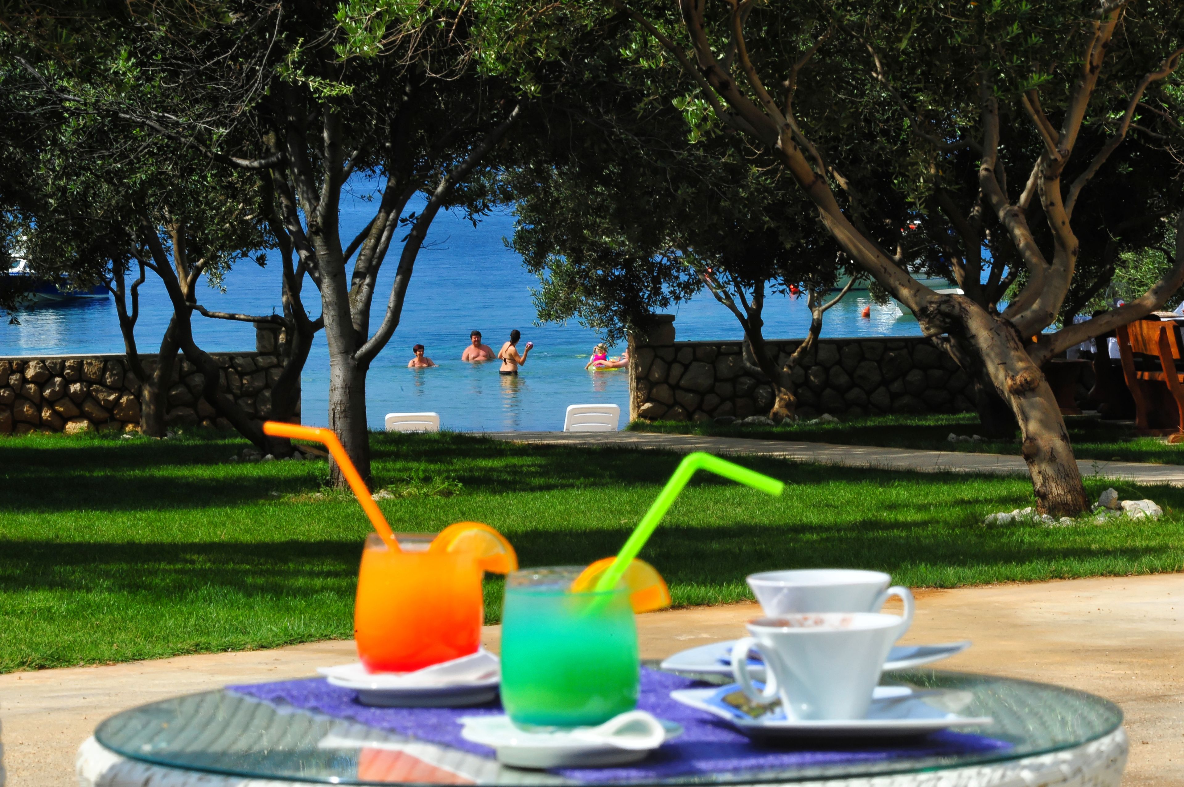 A poolside area with a table set for drinks and a view of the pool and people swimming.