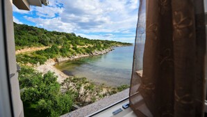 Vista desde una ventana sobre un paisaje costero con vegetación y cielo despejado.