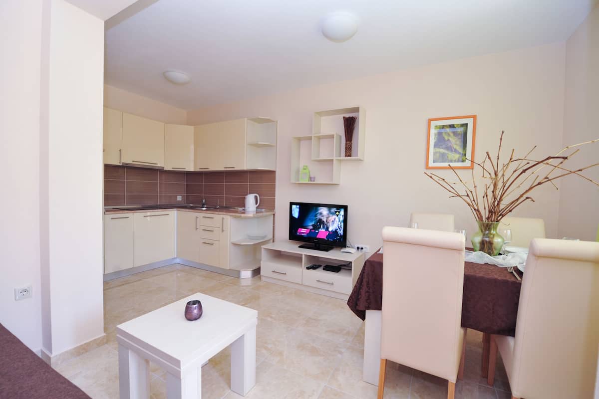 A modern kitchen with white cabinets, a dining area with a table and chairs, and a TV on a stand.