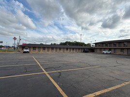 Un motel con estacionamiento, un edificio de una sola planta y un letrero visible para un restaurante.
