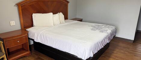 A bedroom with a wooden headboard, a bed with white bedding, a nightstand, and a wooden floor.