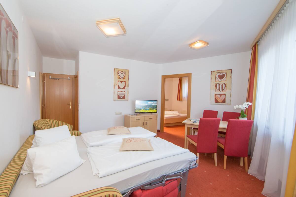 A hotel room with two beds, a TV, a desk with a chair, and a dining area.