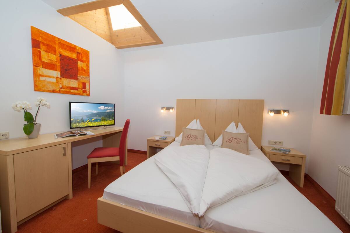 A hotel room with a bed, desk, chair, and a television.