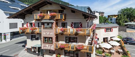 A hotel with multiple balconies adorned with flower boxes, a paved outdoor area with tables and chairs, and a clear view of the surrounding landscape.