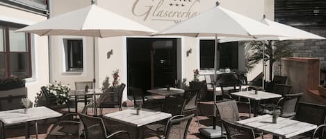 An outdoor patio area with tables and chairs, a sign reading "Hotel Glaserhaus," and a building with a balcony and windows.