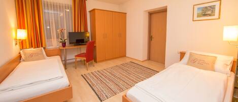 A hotel room with two single beds, a desk with a chair, a TV, and a wardrobe.