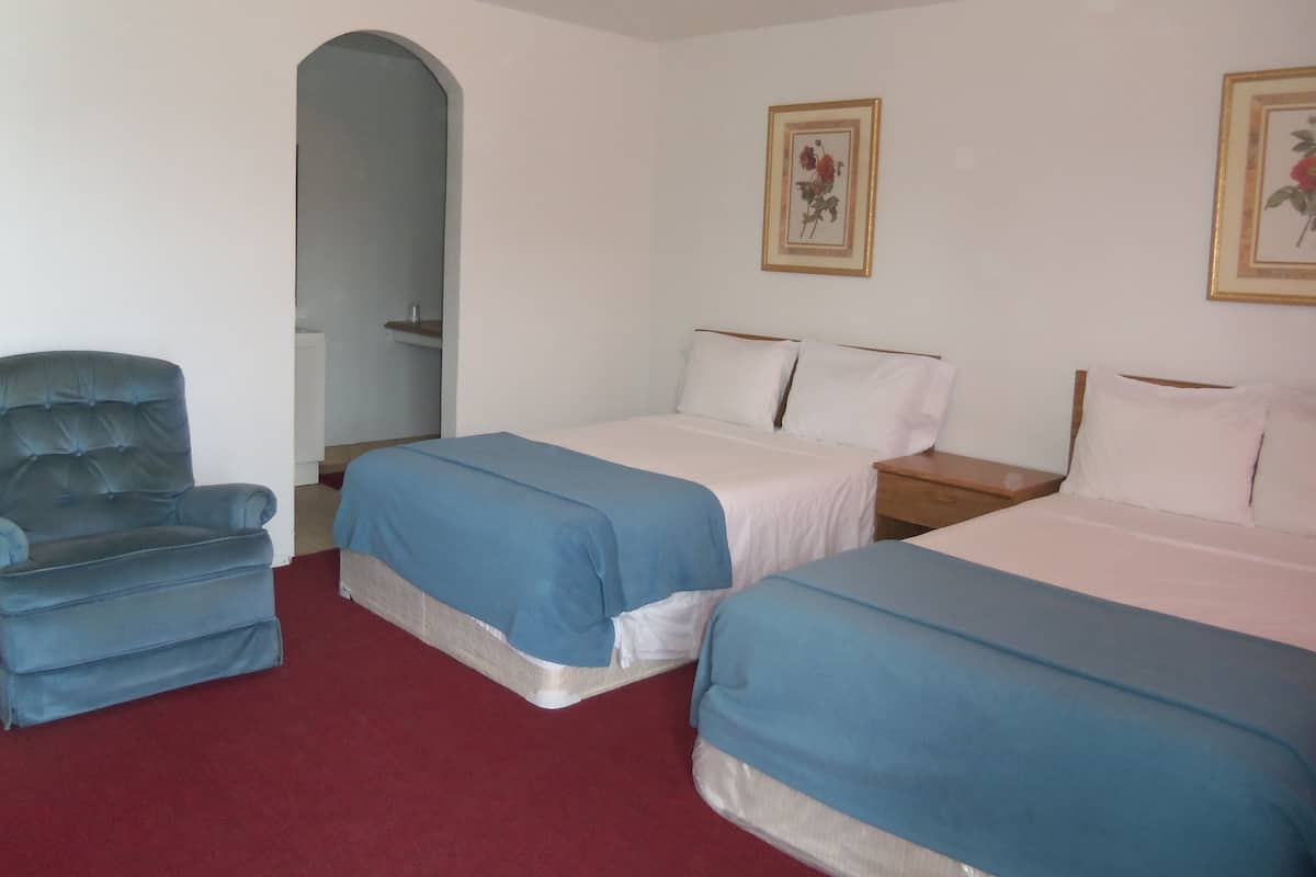 A hotel room with two single beds, a blue armchair, and a wooden nightstand.