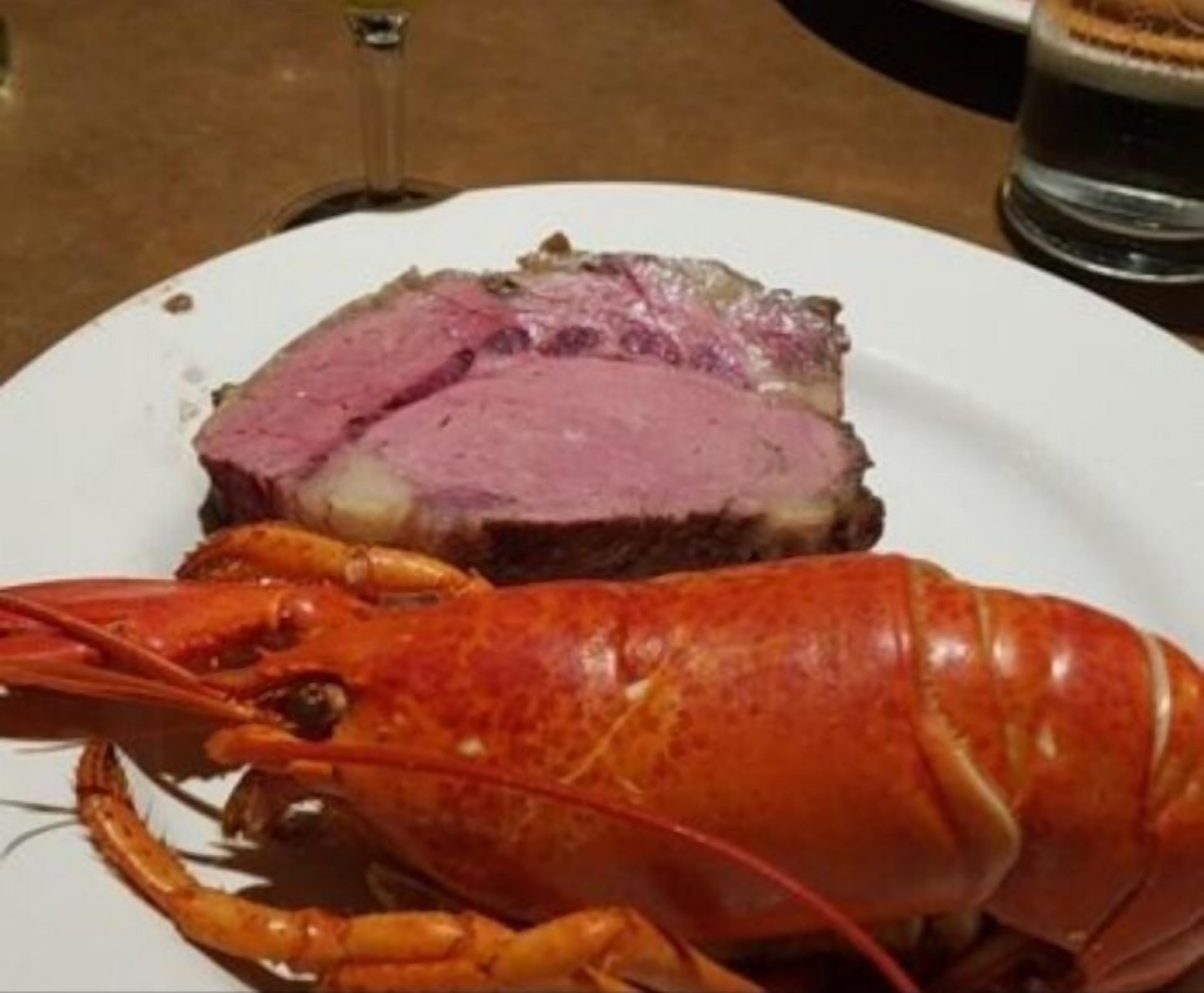 A plate with a lobster and a slice of meat, possibly beef, on a white plate.
