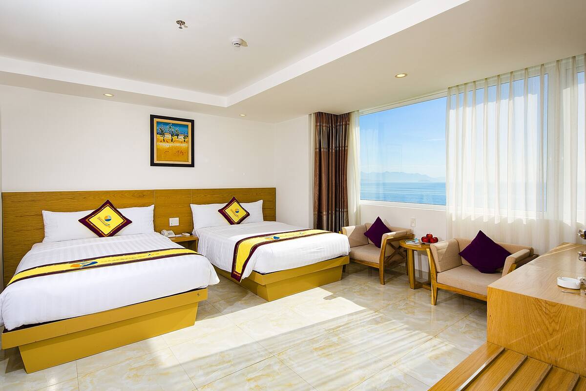 A hotel room with two beds, a sofa, a small table, and a view of the sea.